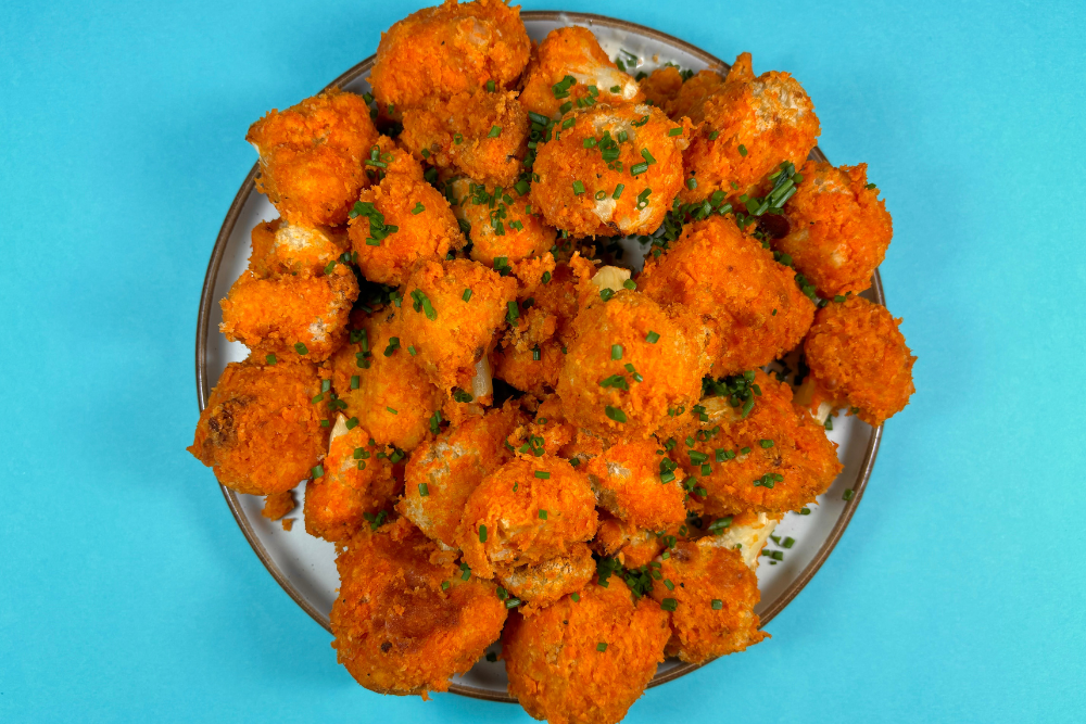  A blue plate with buffalo hot sauce covered cauliflower wings, with a side of Ranch Mayo as a dip on the side. 