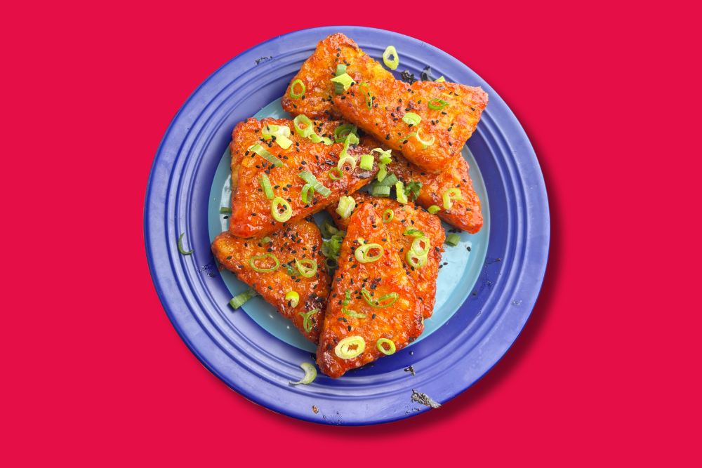  a blue plate with hash browns on top that are covered in Honey Sriracha and topped with spring onions and nigella seeds 