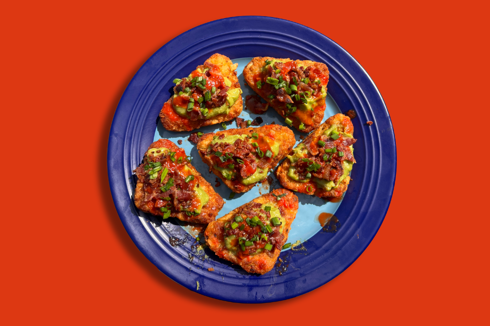  a blue plate with hash browns on top that are covered in Honey Sriracha and topped with spring onions and nigella seeds 